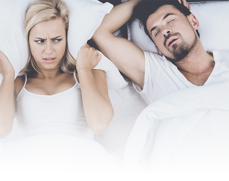 A woman in bed covering her ears while her husband snores